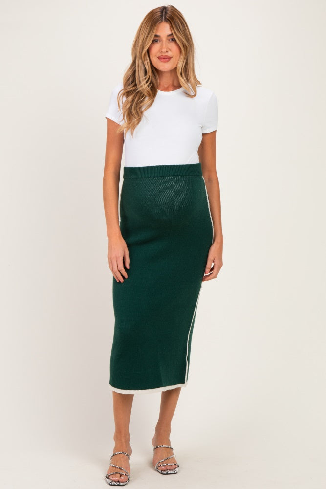 woman wearing a white short sleeve top and a green knit maternity skirt with side detail, showcasing her baby bump