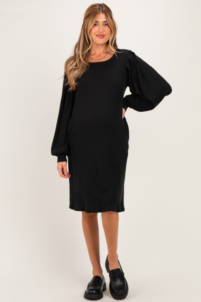 woman wearing a black maternity dress with balloon sleeves and side pockets, showcasing her baby bump