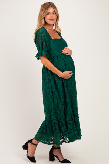 woman wearing a dark green lace maternity dress with short sleeves and a tiered hem, holding her baby bump
