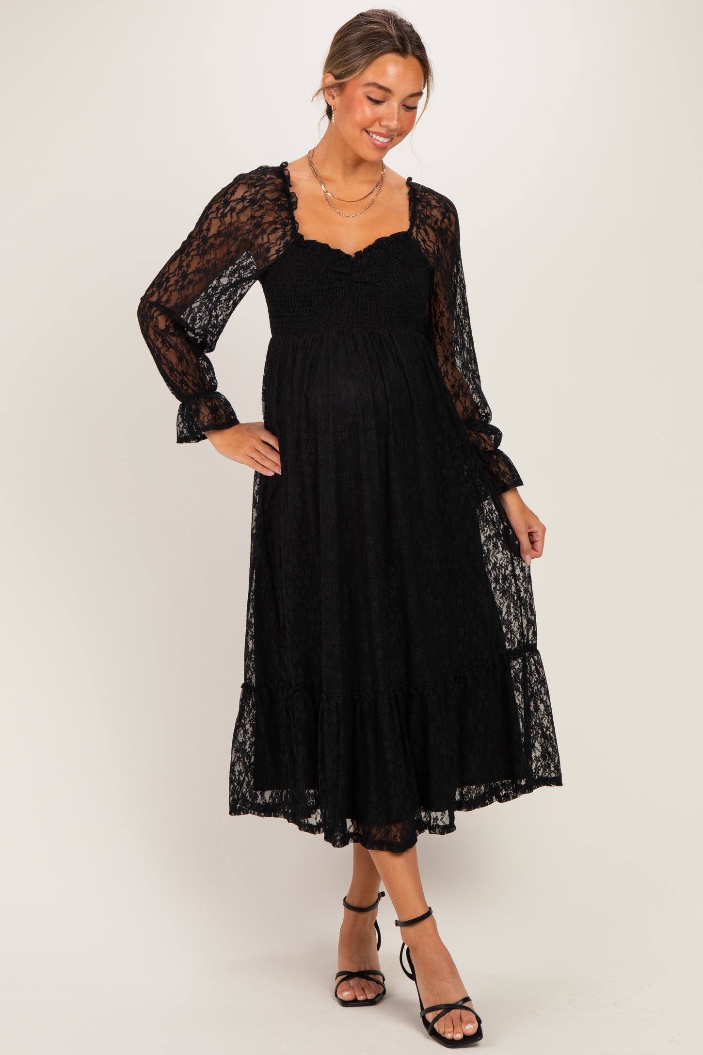 woman wearing a black lace long sleeve maternity dress with a smocked bodice and ruffled hem, baby bump visible