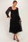 woman wearing a black lace long sleeve maternity dress with a smocked bodice and ruffled hem, baby bump visible