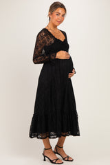 woman wearing a black lace maternity dress with long sleeves and a tiered skirt, cradling her baby bump