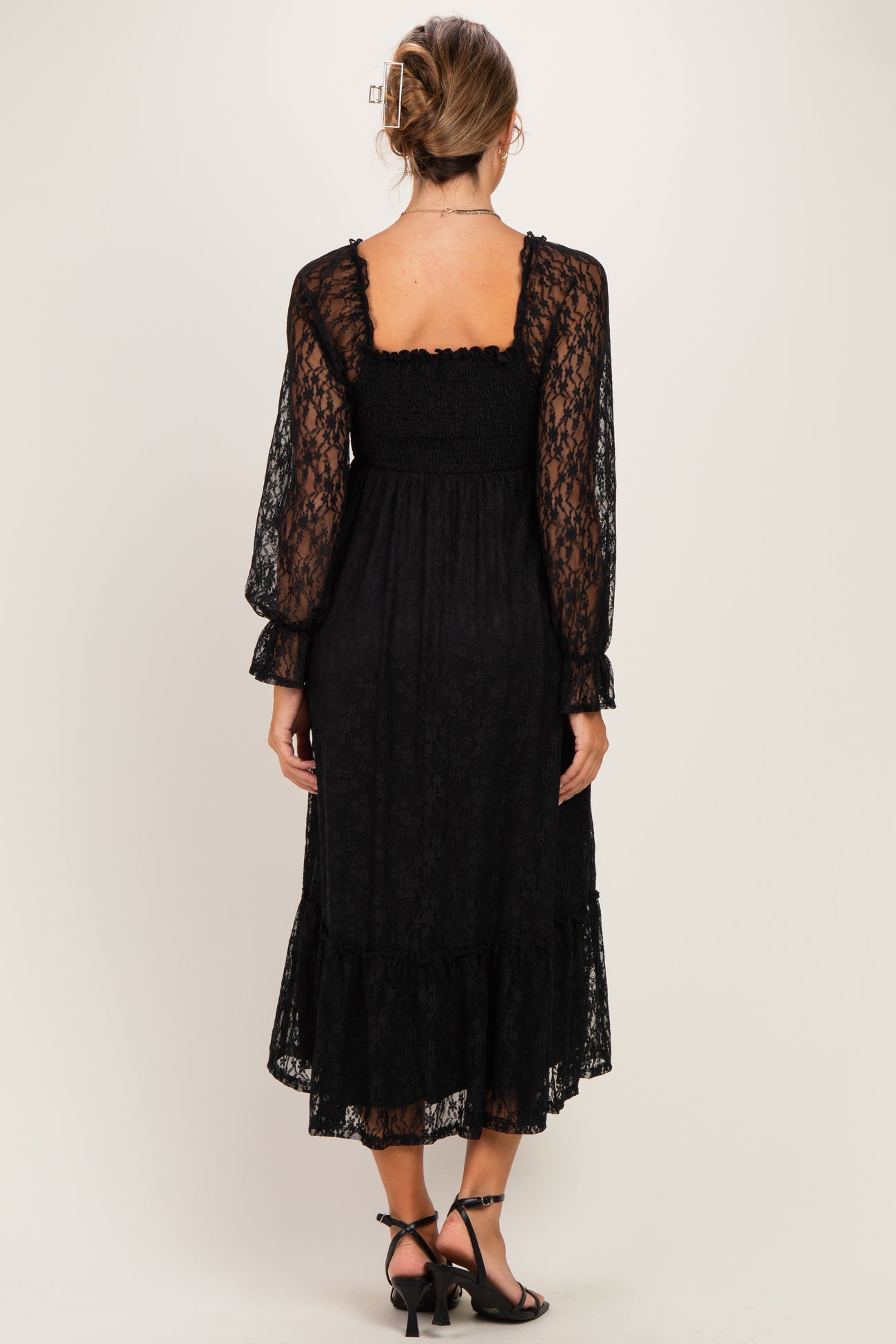 woman wearing a black lace maternity dress with long puff sleeves and a ruffled hem, showing a relaxed fit