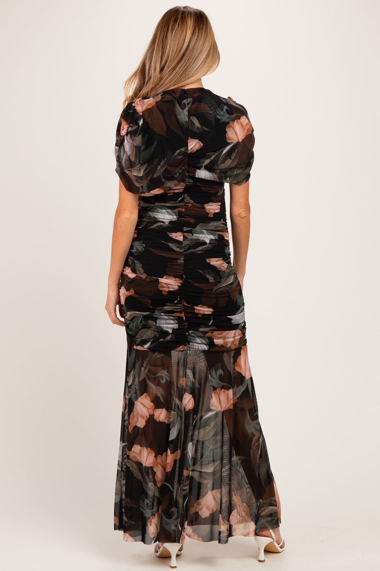 woman wearing a black floral maternity maxi dress with ruched detailing and puff sleeves, showing a baby bump from the back