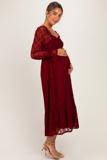 woman wearing a burgundy lace maternity dress with long sleeves and a ruffled hem, holding her baby bump