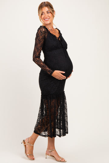 woman wearing a black lace maternity dress with long sleeves and a ruffled hem, smiling and showing her baby bump