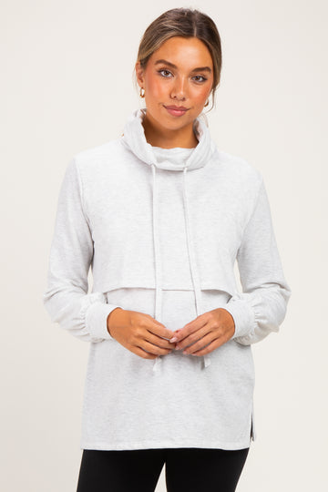 woman wearing a light grey maternity pullover with a cowl neck and drawstrings, featuring a layered look and side slits