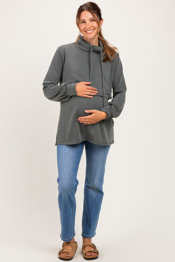 woman wearing a dark gray maternity hoodie with a cowl neck and holding her baby bump while standing in casual blue jeans