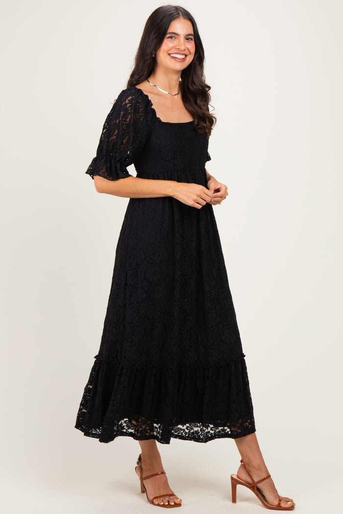woman wearing a black lace maxi dress with short puff sleeves and a tiered hemline, standing sideways