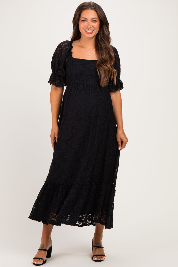 woman wearing a black lace maternity dress with puff sleeves and a tiered skirt, showing her baby bump