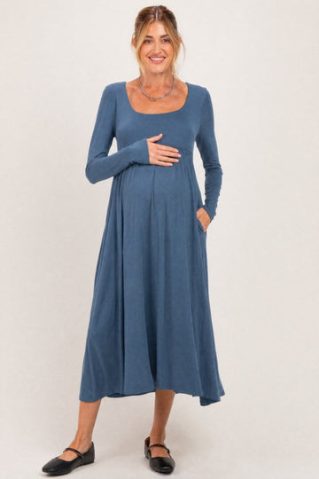woman wearing a blue long sleeve maternity dress with a scoop neckline and pockets, cradling her baby bump