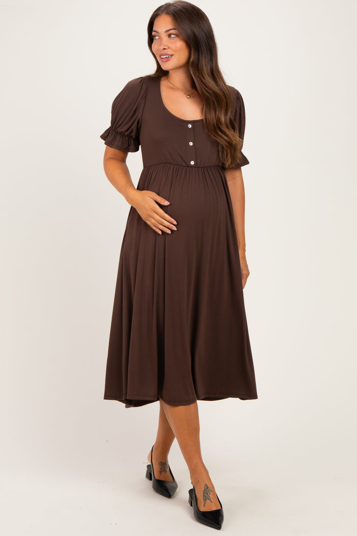 woman wearing a brown maternity dress with short puff sleeves and buttons, gently holding her baby bump