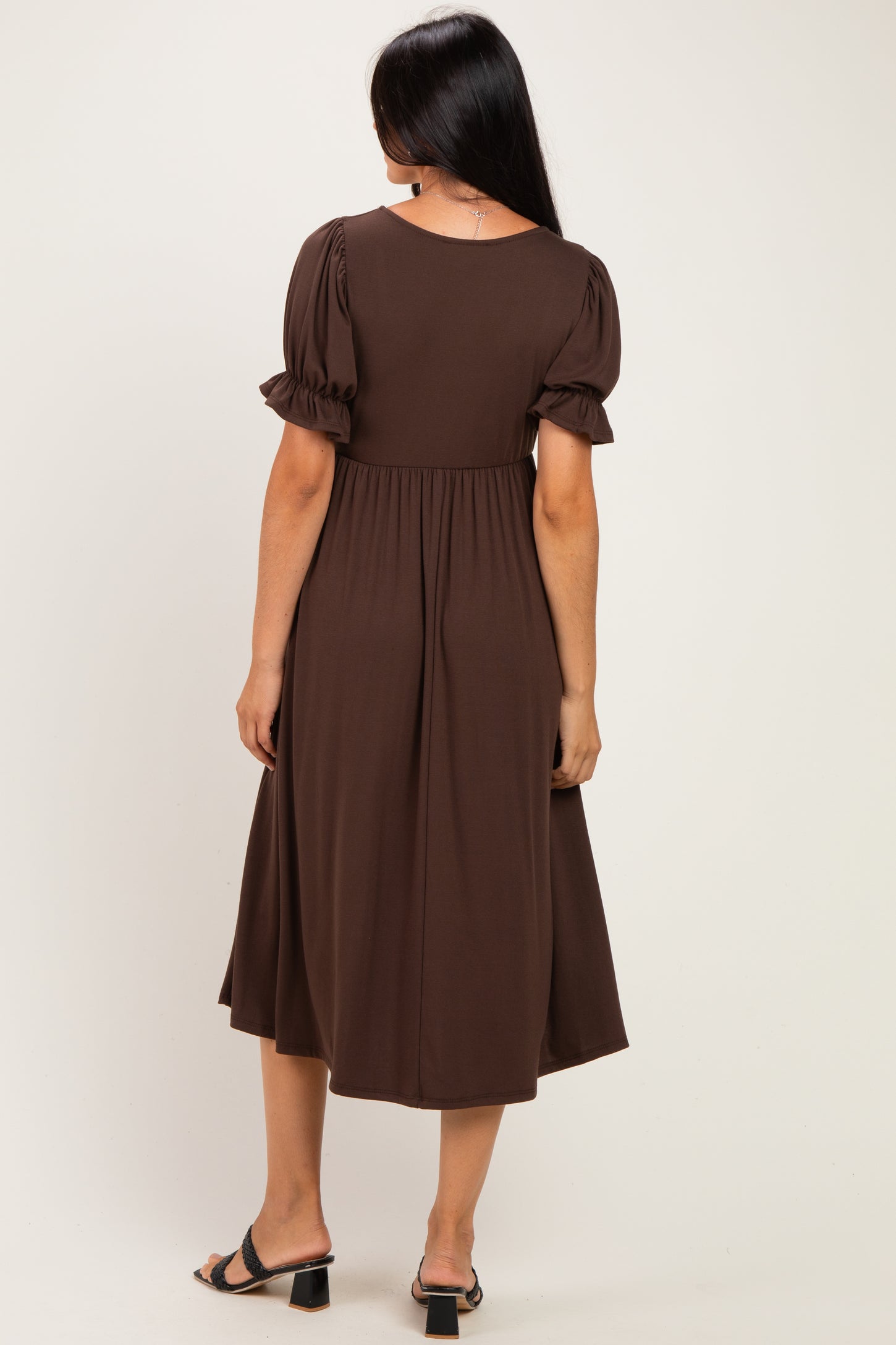 woman wearing a brown midi dress with puff sleeves and a fitted waist, seen from the back