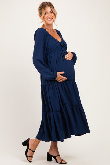 woman wearing a navy blue maternity dress with long puff sleeves and tiered skirt, showing her baby bump
