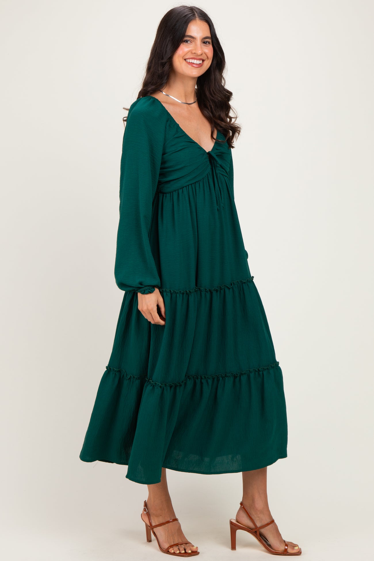 woman wearing a dark green tiered maxi dress with long sleeves and a v-neckline, standing sideways