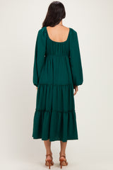 woman wearing a dark green tiered midi dress with long puff sleeves and a low back
