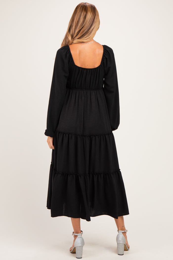 woman wearing a black tiered maternity dress with long sleeves and a square back design