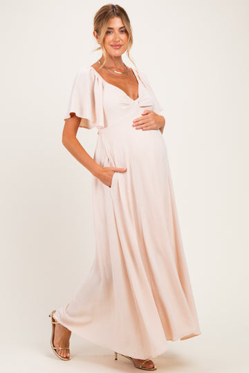 woman wearing a light pink maternity maxi dress with short flutter sleeves and pockets, gently cradling her baby bump