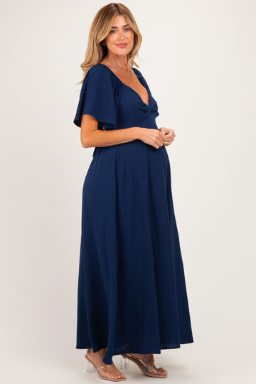 woman wearing a navy blue maxi maternity dress with short flutter sleeves and a v-neck, showing her baby bump