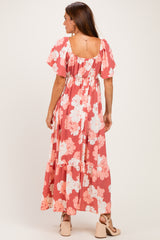 woman wearing a coral floral maxi dress with flutter sleeves and a tiered hem from the back