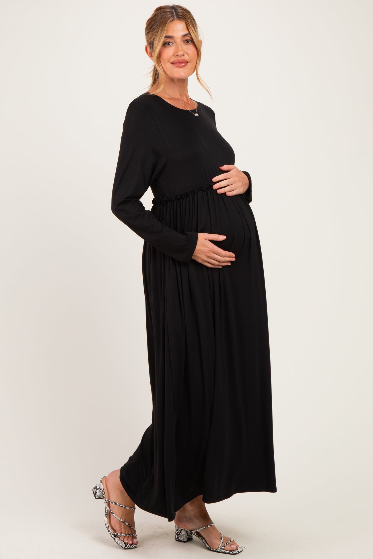 woman wearing a black long sleeve maternity dress with gathered waist, holding her baby bump