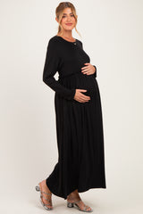 woman wearing a black long sleeve maternity dress with gathered waist, holding her baby bump