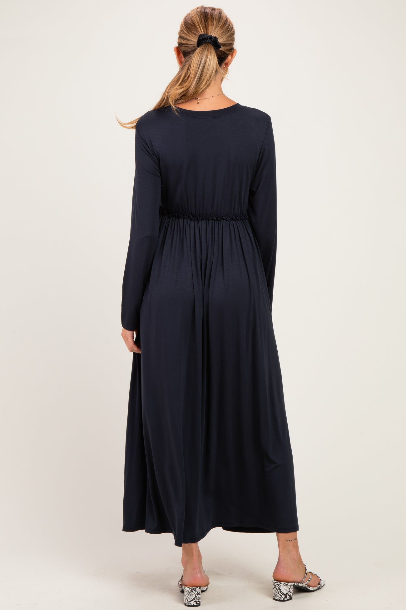 woman wearing a navy blue long sleeve maternity dress with an elastic waistband, showing a flowing silhouette from the back