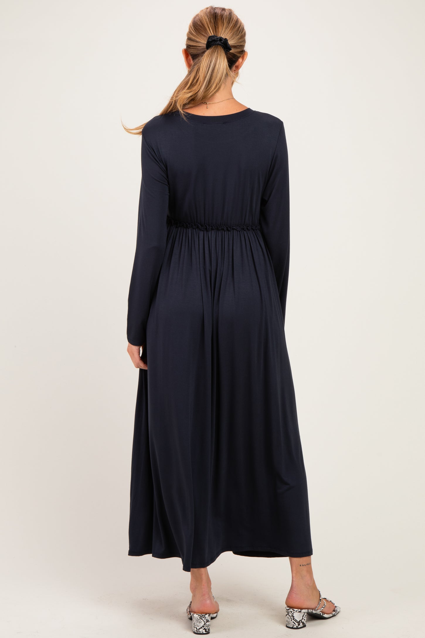 woman wearing a navy blue long sleeve maternity dress with an elastic waistband, showing a flowing silhouette from the back