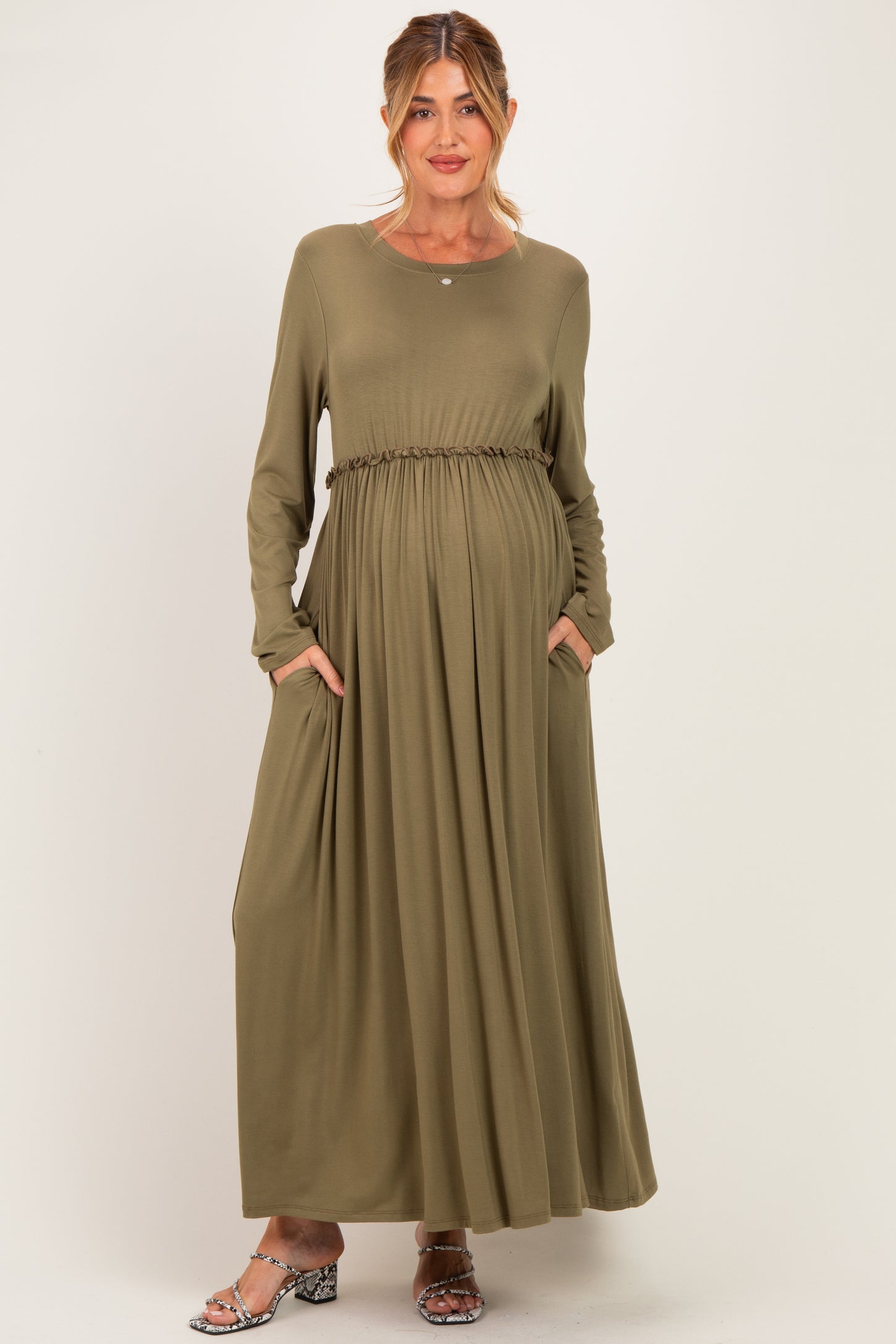 woman wearing an olive green long sleeve maternity dress with a cinched waist and pockets, revealing a baby bump