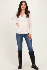 woman wearing a cream long sleeve wrap top with ruching and blue skinny jeans, standing in black knee-high boots