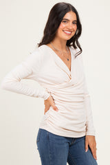 woman wearing a soft beige long sleeve wrap top with ruching detail, paired with blue jeans