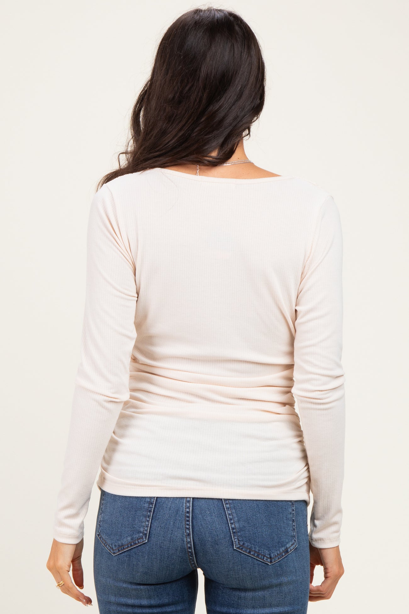 woman wearing a light pink long sleeve ribbed top and blue jeans, viewed from the back
