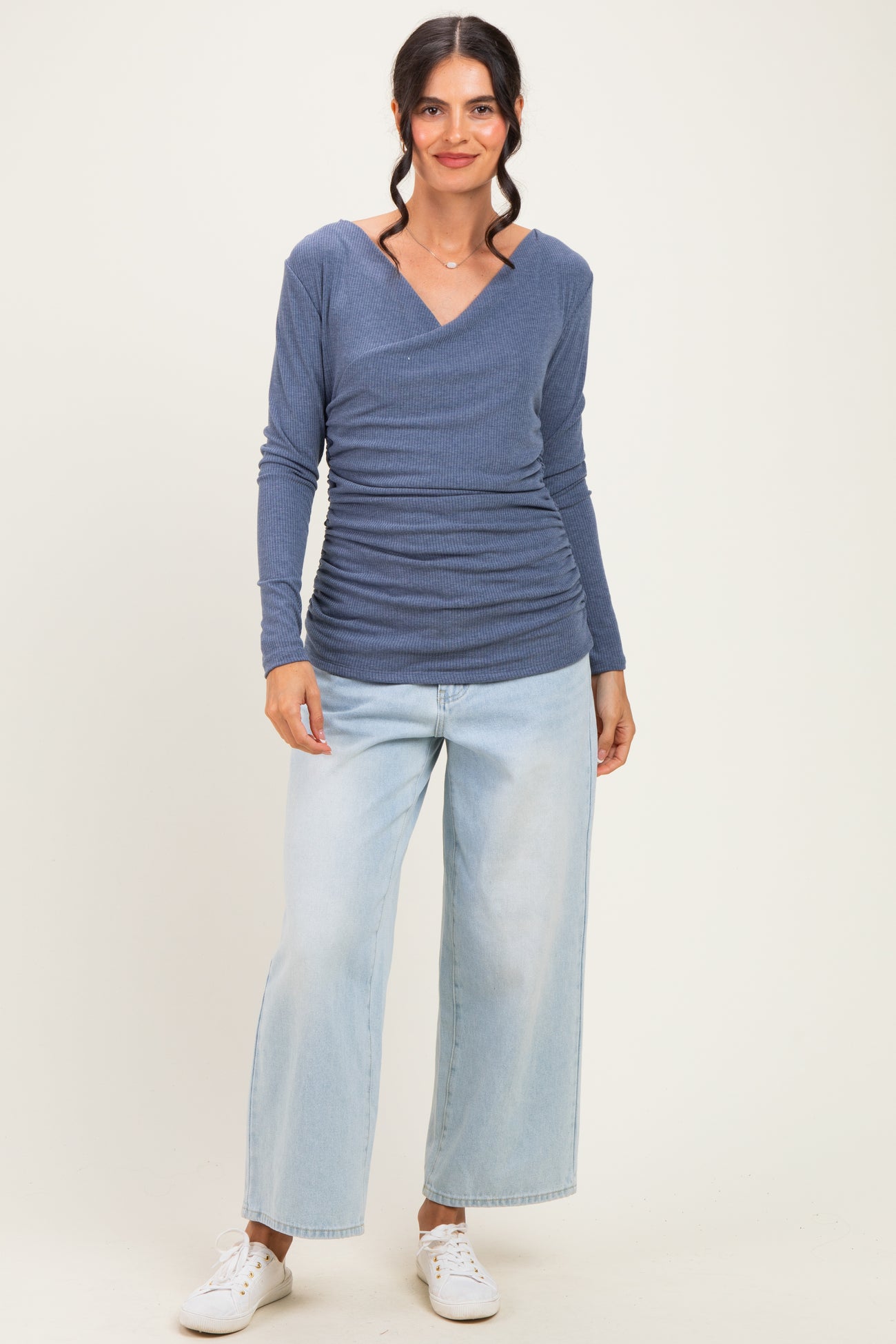 woman wearing a blue long sleeve ruched top with a v-neck and light wash wide-leg jeans