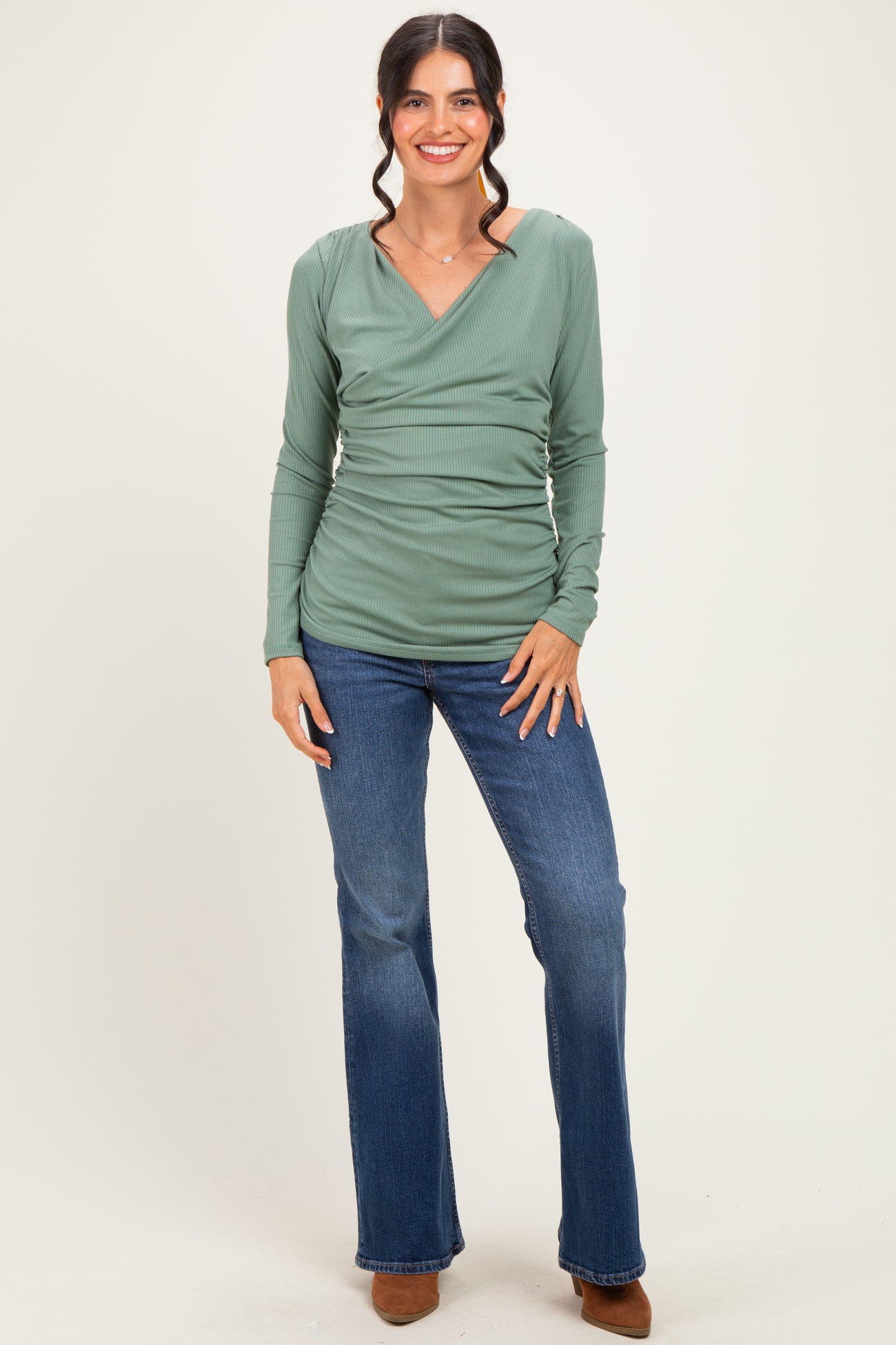 woman wearing a green long sleeve wrap top with vertical ribbing and flared jeans