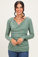 woman wearing a sage green long sleeve top with a wrap neckline and gathered sides, smiling at the camera