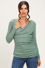 woman wearing a green long sleeve fitted top with a v-neck and gathered side detail, paired with blue jeans