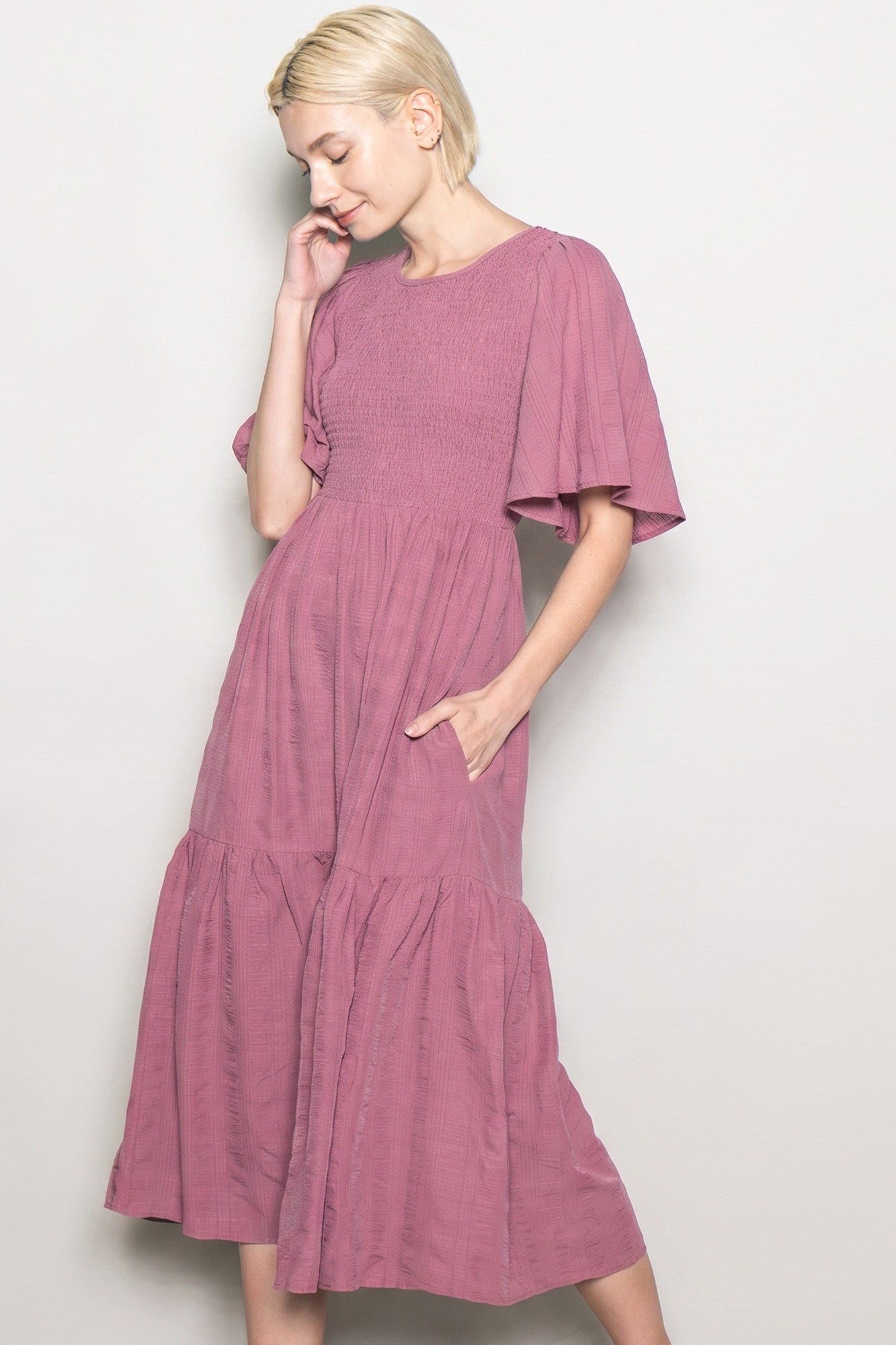 woman wearing a mauve smocked tiered midi dress with short flutter sleeves and pockets