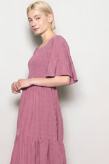 woman wearing a light pink smocked maxi dress with flutter sleeves and a tiered hemline