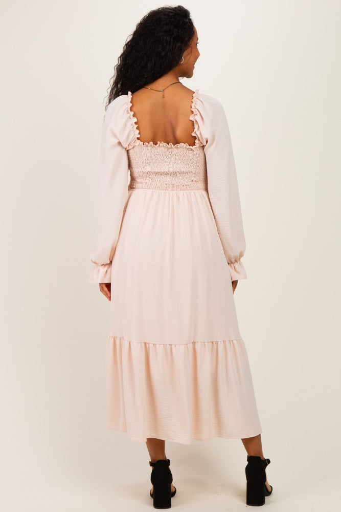 woman wearing a light pink maternity dress with a smocked bodice and long sleeves, showing the back view