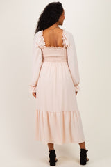 woman wearing a light pink maternity dress with a smocked bodice and long sleeves, showing the back view