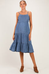 woman wearing a denim blue maternity dress with tiered ruffles and spaghetti straps, standing with a relaxed pose