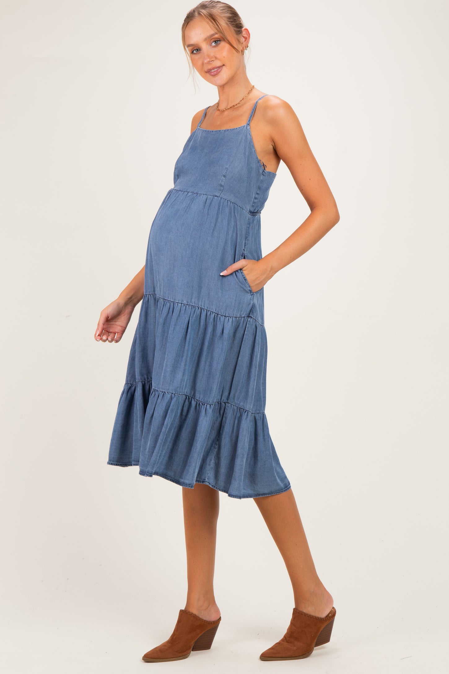 woman wearing a denim blue maternity dress with tiered ruffles and pockets, showcasing her baby bump