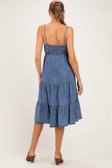 woman wearing a blue denim maternity dress with a smocked bodice and tiered skirt, showing a baby bump from behind