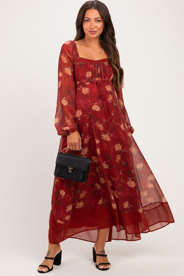 woman wearing a burgundy floral maxi maternity dress with long sleeves and a fitted bodice, holding a black handbag