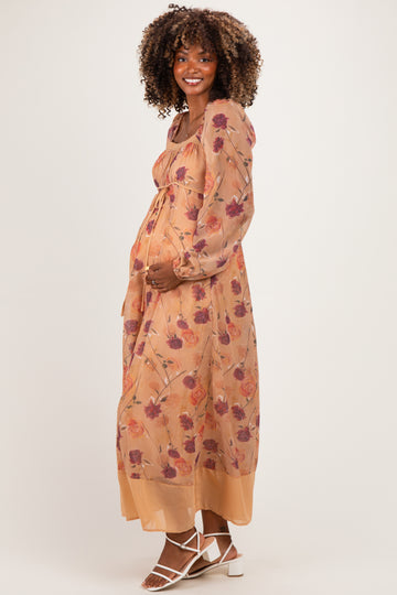 woman wearing a floral maternity maxi dress with long sleeves and a tied waist, holding her baby bump