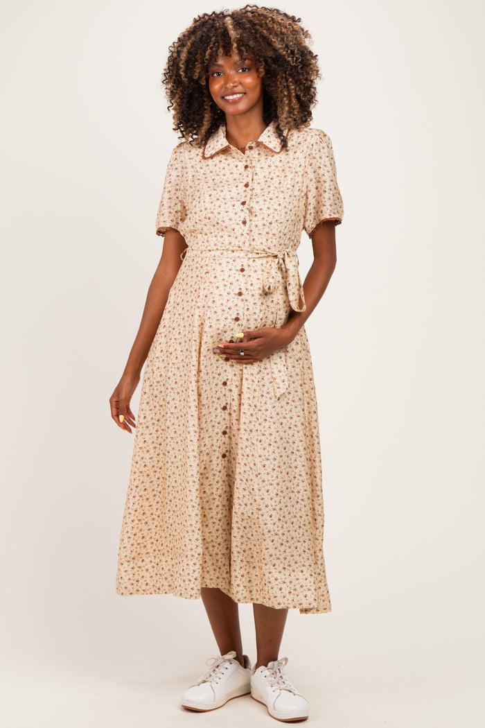 woman wearing a beige floral midi maternity dress with buttons and a tie waist, holding her baby bump