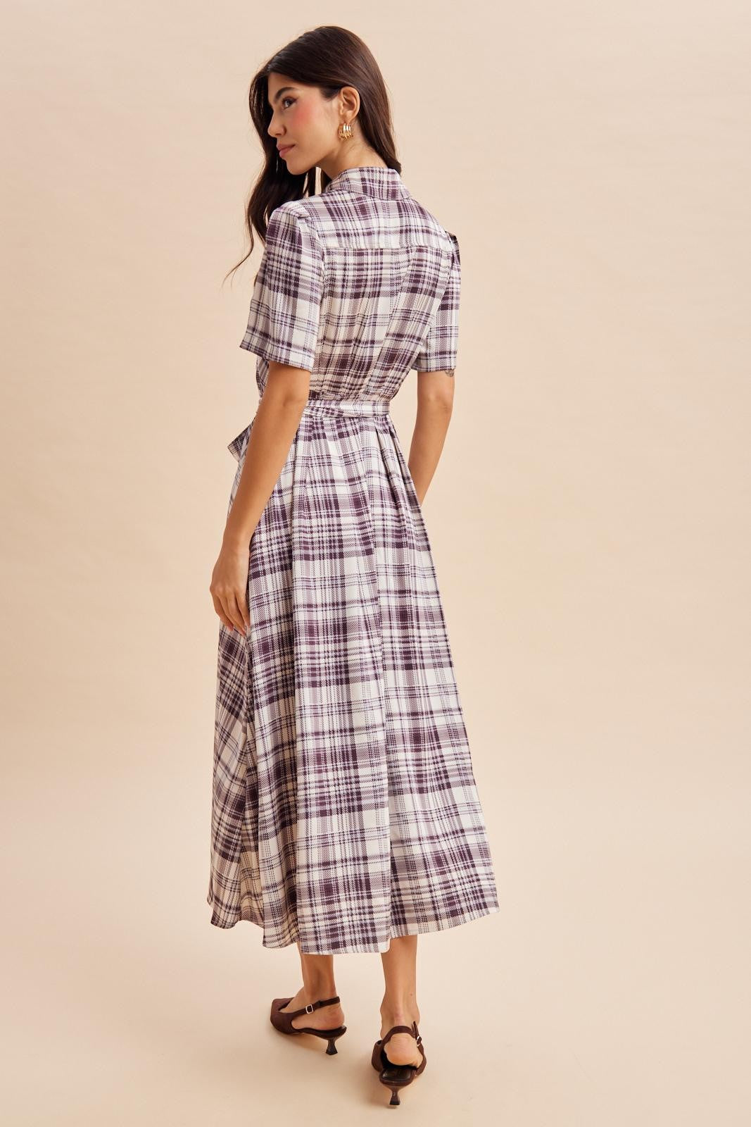 woman wearing a short sleeve purple and white plaid midi dress with a tie waist, viewed from the back