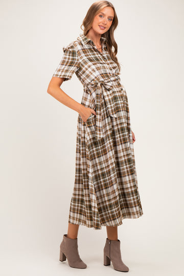 woman wearing a brown and white plaid maternity dress with a tie waist and pockets, showing her baby bump