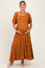 woman wearing a rust-colored maternity maxi dress with puff sleeves and floral embroidery, cradling her baby bump