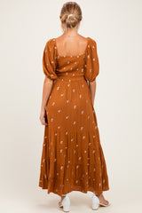 woman wearing a brown maternity maxi dress with floral embroidery and puffy sleeves, seen from the back